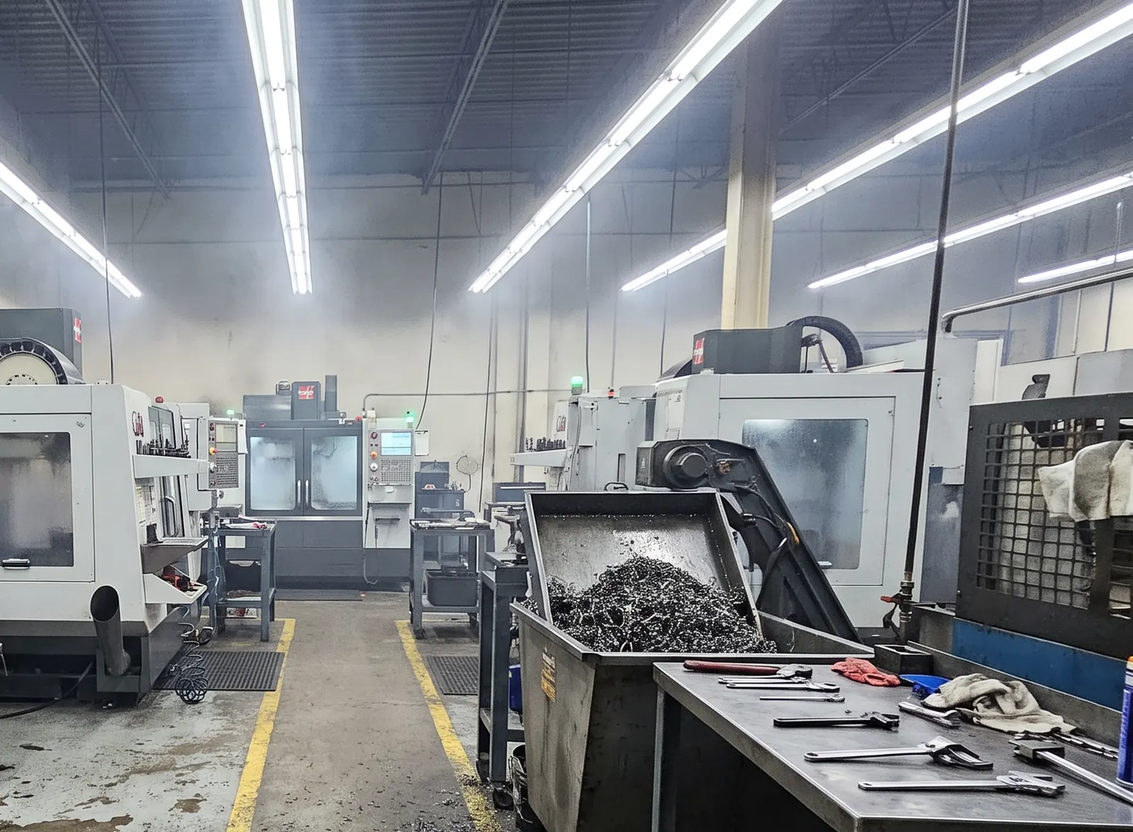 Intérieur de l'atelier : centre d'usinage CNC, tour conventionnel et scie à ruban alignés le long d'une ligne jaune